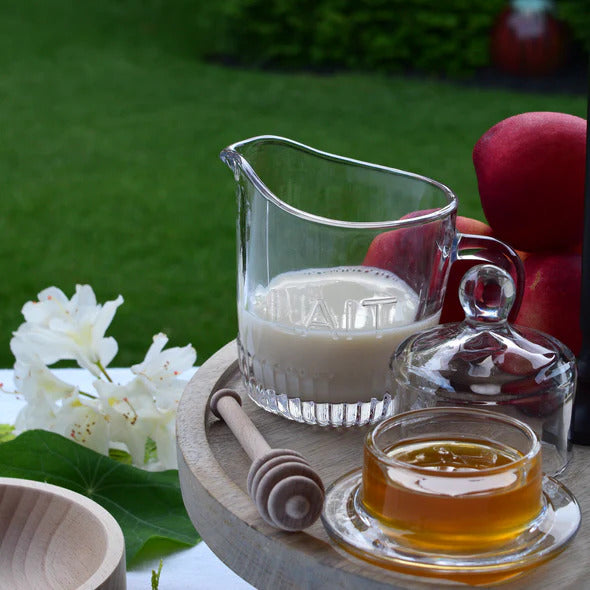 Clear vintage-style ribbed glass sugar bowl with a matching dome lid and round knob top, embossed with the word SUCRE, resting on a rustic wood table.